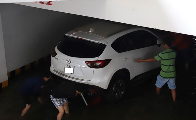 Một chiếc Mazda CX - 5 bị ngâm nước trong tầng hầm. Người dân kiểm tra xe, trong khi các nhân viên cứu hộ tiến hành các thao tác để kích xe liên phục vụ việc kéo xe ra ngoài